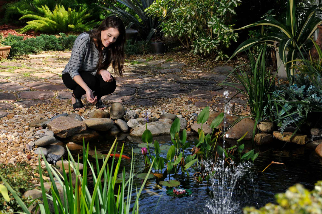 Woman crouching by a small pond with plants and rocks in a garden setting